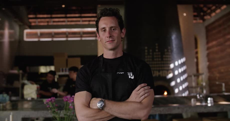 Restaurant worker poses while coworkers use pasta machine in the background