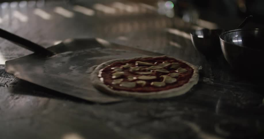 A person uses a peel to pick up a pizza from the kitchen table at a restaurant