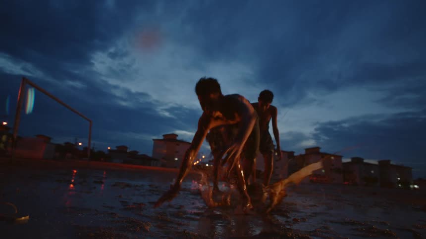 Group of young shirtless barefoot boys playing soccer on a park at evening