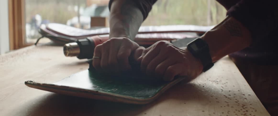 Man uses his hands to peel a griptape layer from the surface of a disassembled skateboard