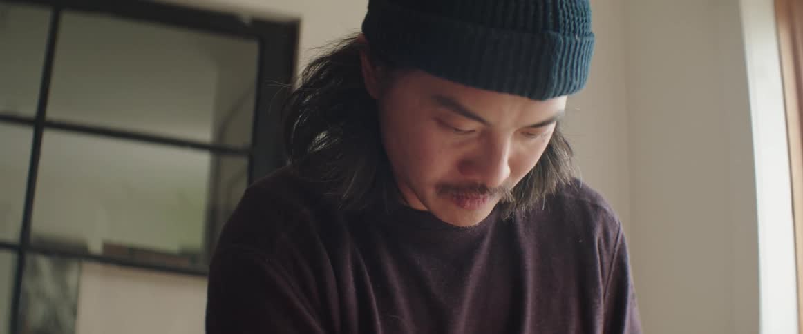 Man with long hair and mustache wearing a beanie working at home