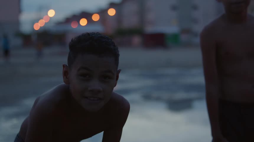 Two boys stand near reflective water across from apartment buildings under a cloudy sky
