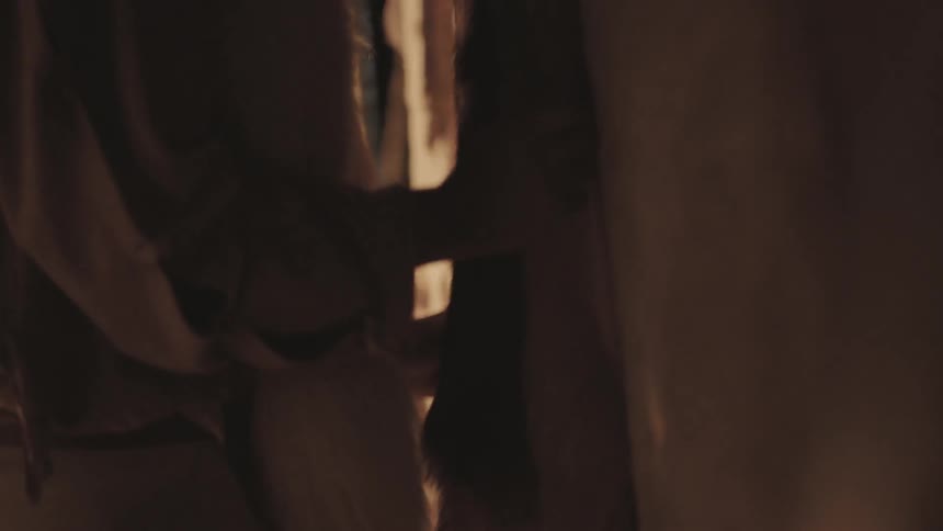 A woman traces her hand against some hanging hides at night