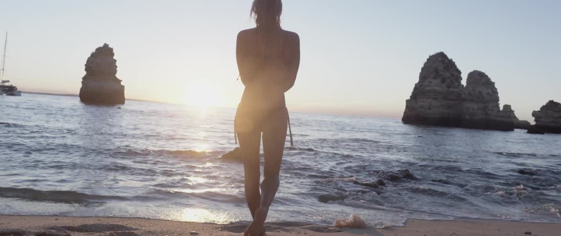 Woman walking towards the water on a rocky beach at sunset