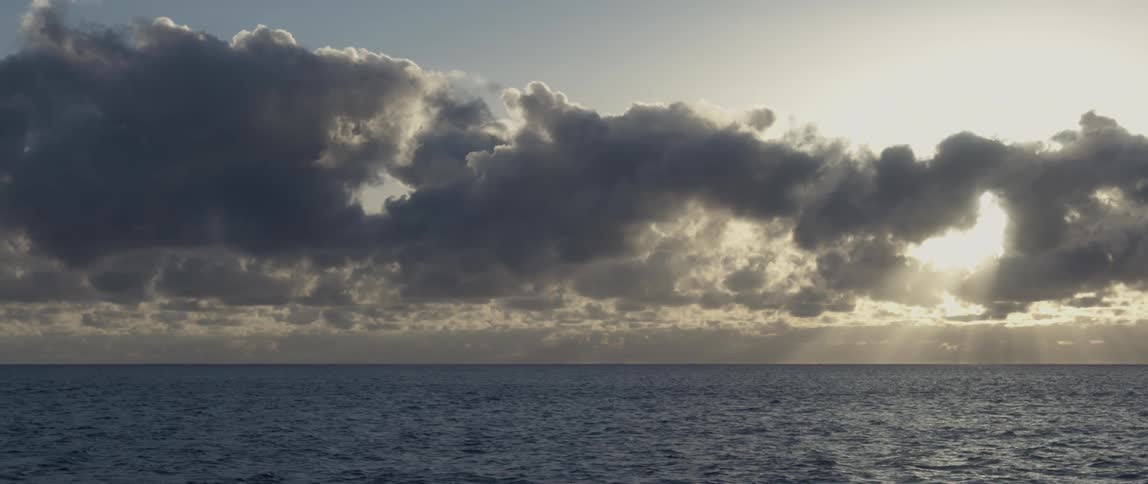 Gray clouds hang over an ocean as sun rays peak through