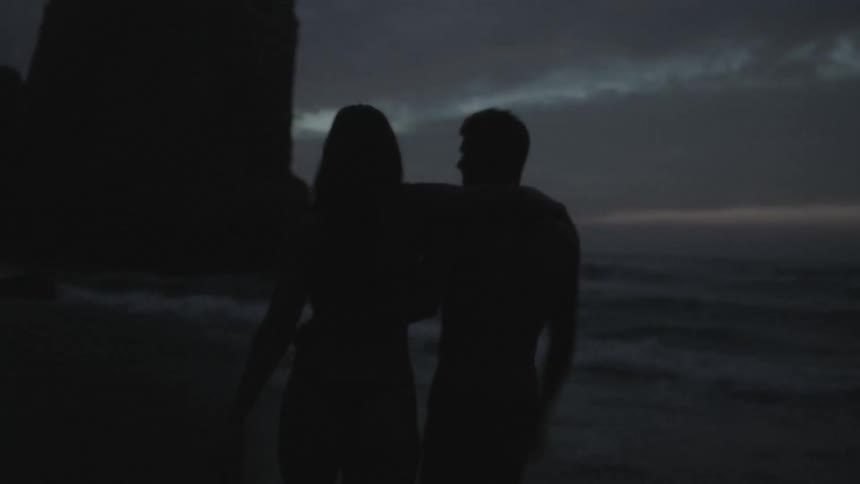 A couple walking along the beach as night falls