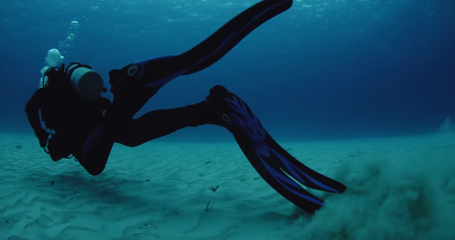 A diver swims with his flippers churning up sand on the seafloor