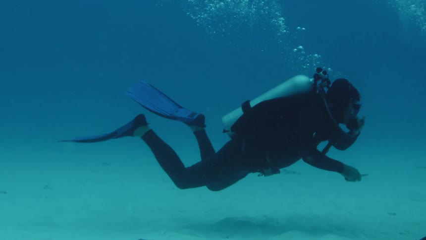 A scuba diver swimming around slowly and making bubbles
