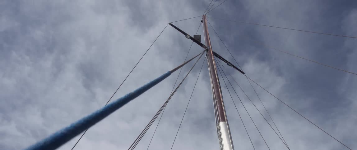Looking up towards the top of the mast of a sail ship against the clouds