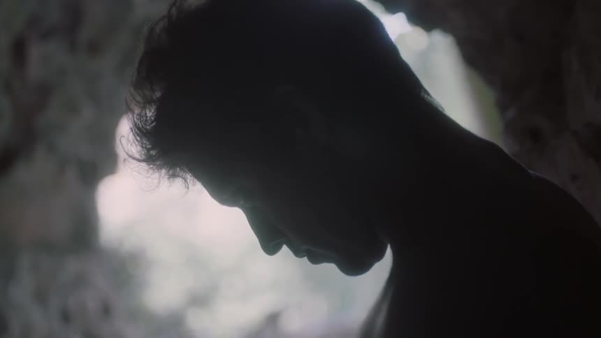 A person raises their head from looking down while standing in what appears to be a cave