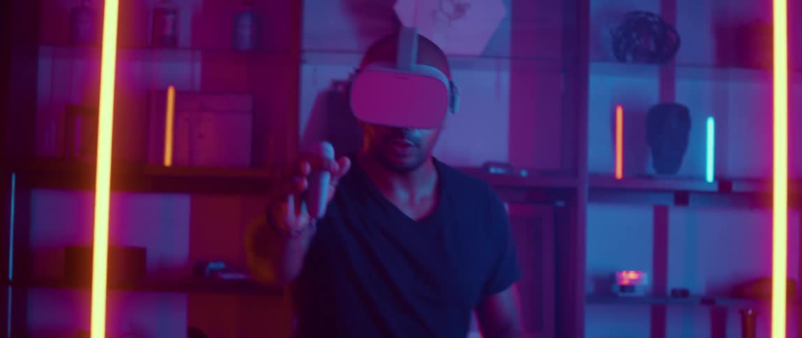 A man playing a virtual reality game at home pretends to draw a weapon from his pocket and aims it