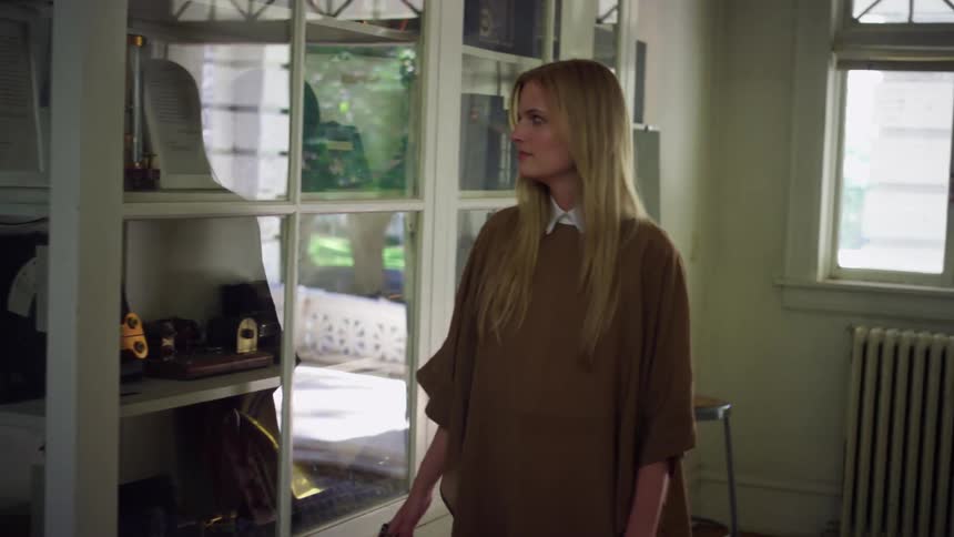 A woman at home walks backwards and looks in to a glass cabinet