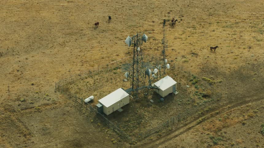 Wild horses graze outside a cell phone tower structure high on a hilltop in rural America as seen from this high altitude aerial shot