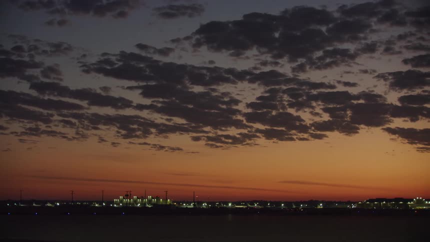 City lights glow at daybreak along the coast under a red and purple cloud sunrise sky