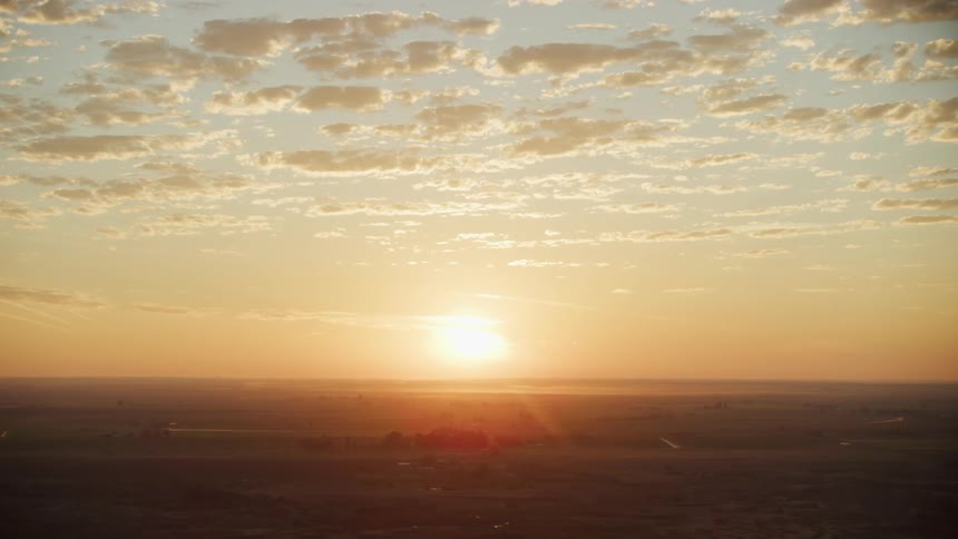 Aerial view of the sun setting on the horizon over the plains in the countryside at evening