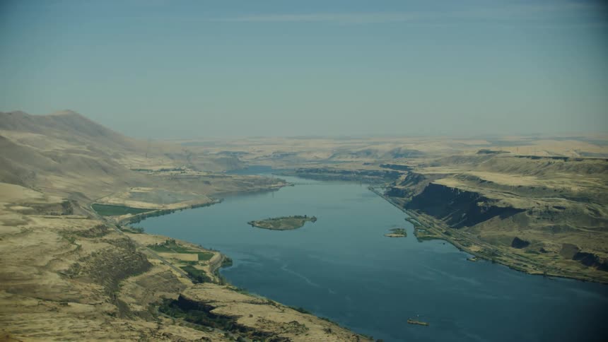 Aerial view of a the Columbia River winding around an extensive desert in warm summer light