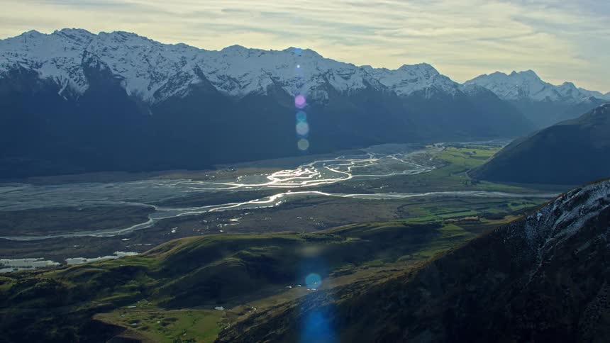 Aerial view of snowy mountain range and valley river with lens flare