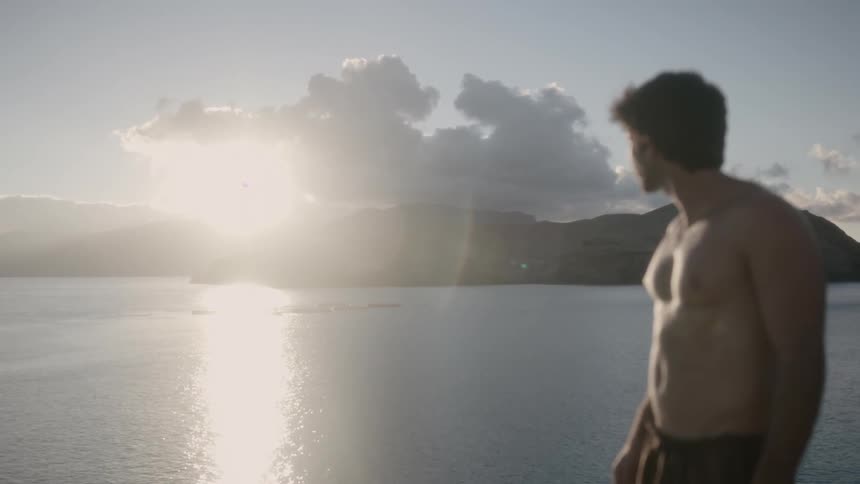 A man looks over the water at a rising sun