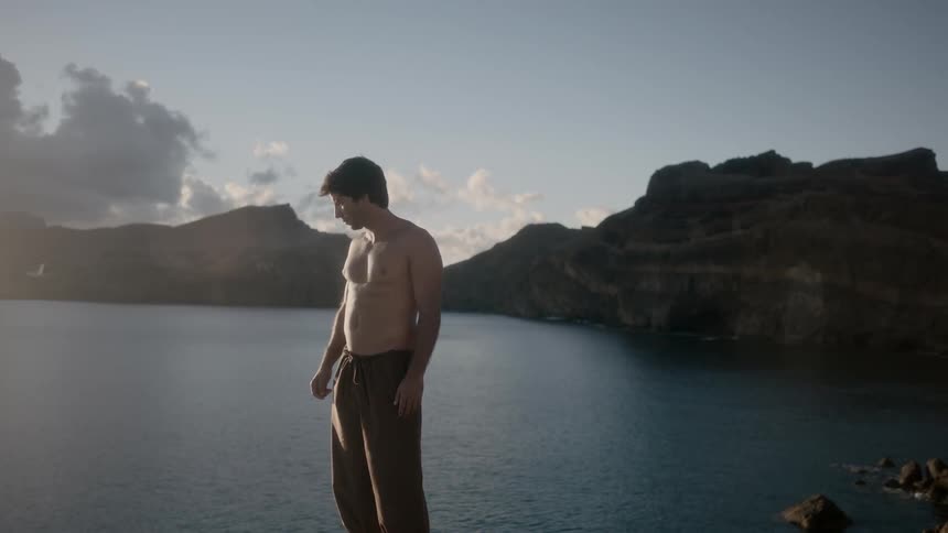 A shirtless man looks out over a body of water