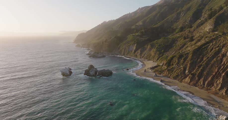 Ocean waves wash upon the shore at the base of tall mountains lining the coastline