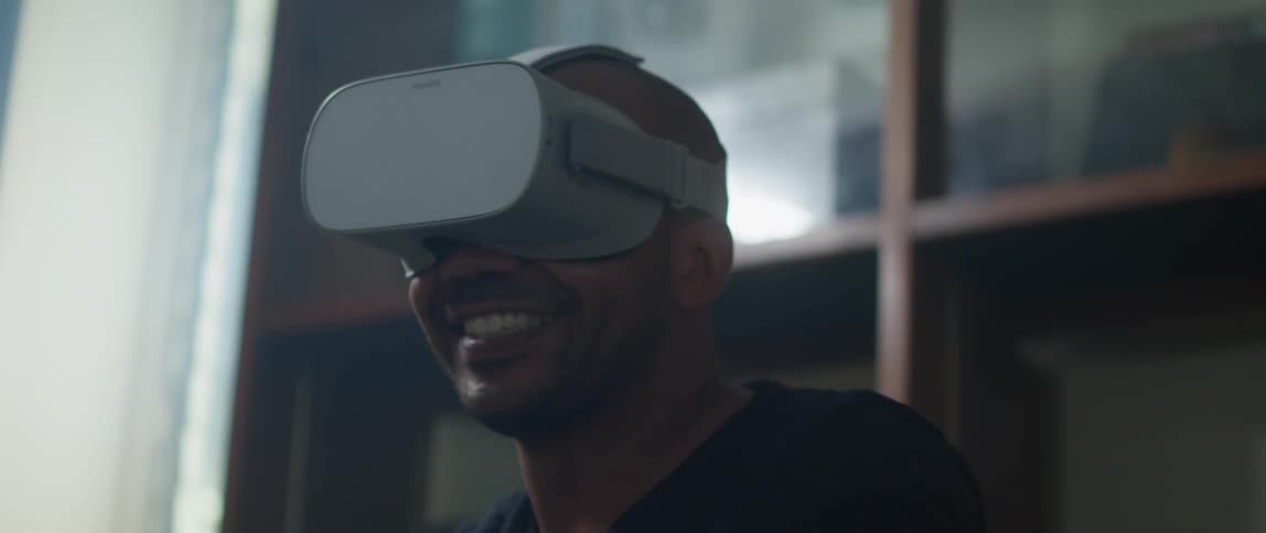 Man with black t shirt and virtual reality headset sits on couch swinging his arm