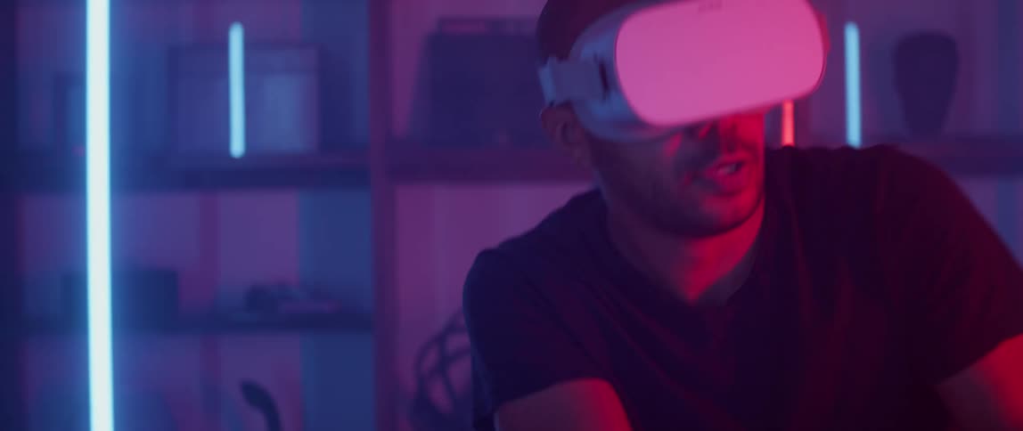 Man gestures energetically while playing virtual game in dim room lit by light bars