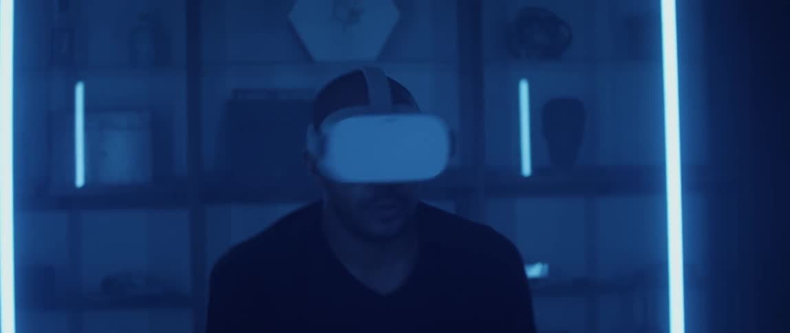 A man wearing a virtual reality headset looks around and aims his controller while playing a game
