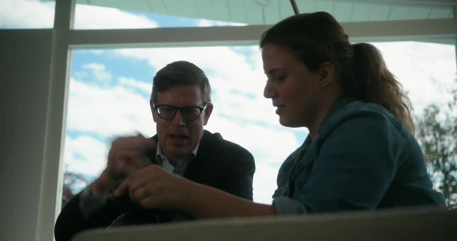 Man wearing glasses and black jacket checks photos on camera with photographer in the living room