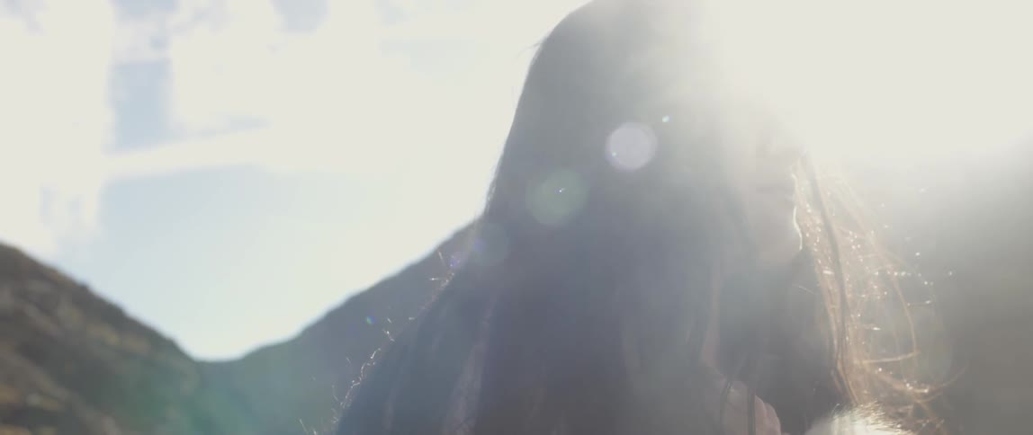 A woman with long hair stands in the sunlight