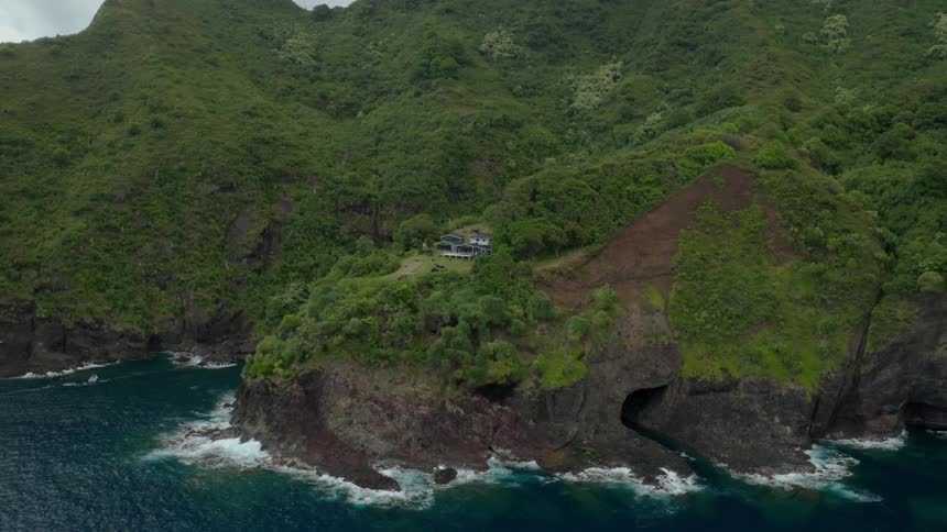 A house sits high up on a mountain above the water