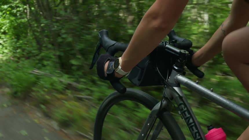 Cyclist pedals along paved path through woods