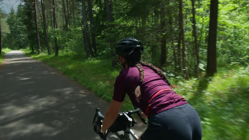 A woman wearing a cycling helmet is riding a bicycle on a bike path through the woods
