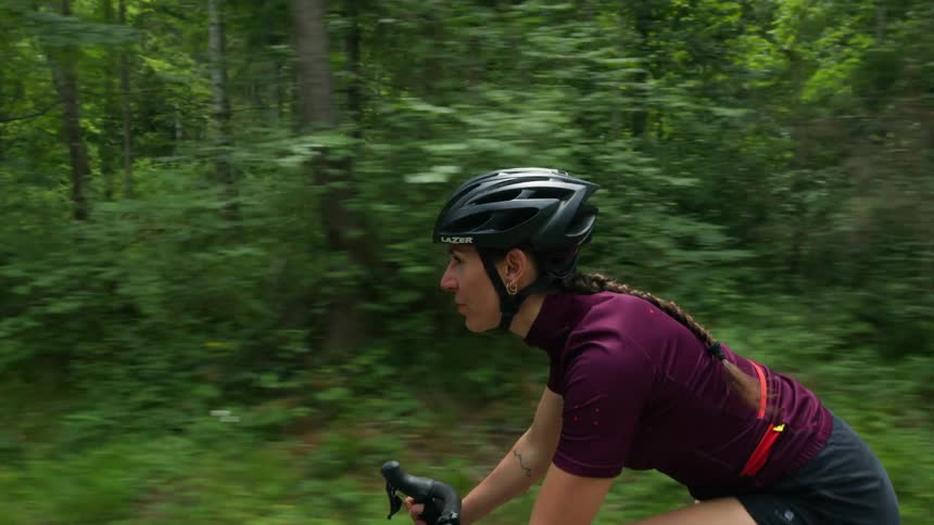 A woman wearing a cycling helmet is riding a bicycle on a bike path through the woods