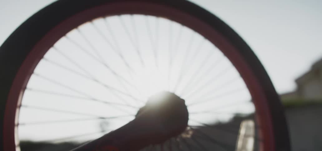 The sun shines brightly upon a bicycle tire on a bike in a neighborhood as a persons hand moves it