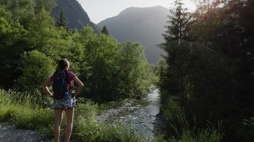 A woman stands by a river in a forest and looks around