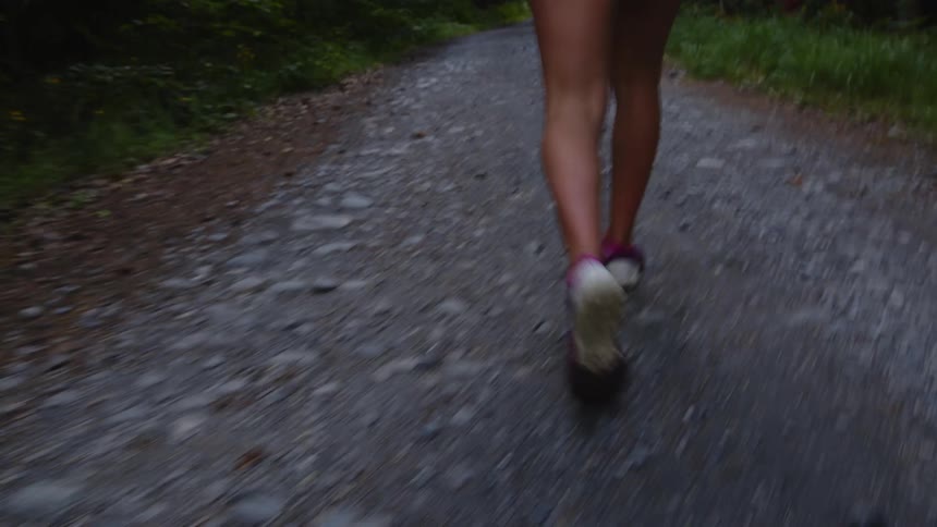 A woman hikes along a narrow paved path through a woodland during the day