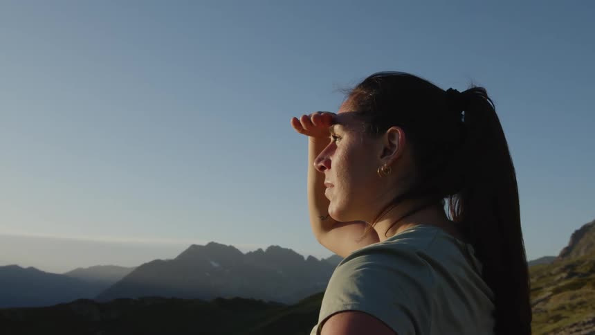 A woman holds her hand above her eyes to block the sun and looks at a mountain range