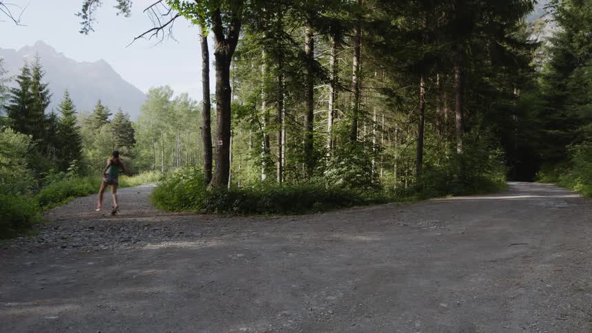 A young white woman is jogging down the road in the forest area