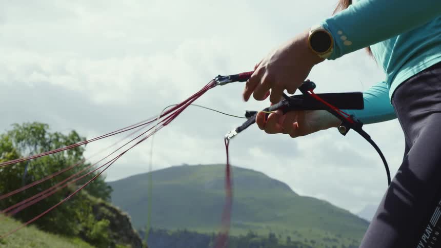 A woman is pulling at paragliding cords on a hill