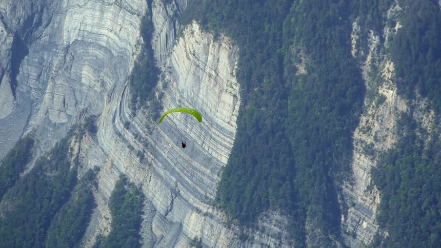 A paraglider is flying inside a canyon with vines and plants growing on the side