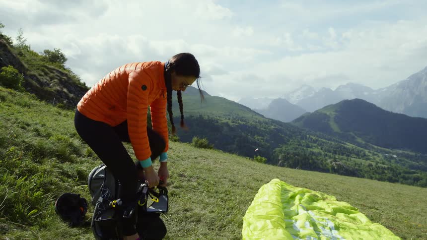 A young white woman is standing on a hill getting ready to paraglide