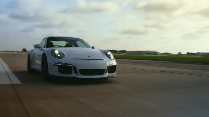 A white porsche speeds down a wide highway strip at daytime