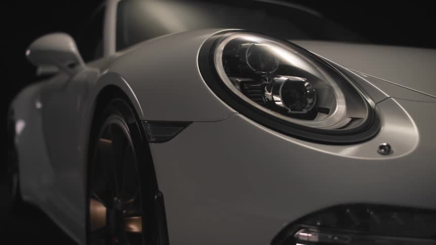 Close up of the front of a white porsche 911 car in a black room