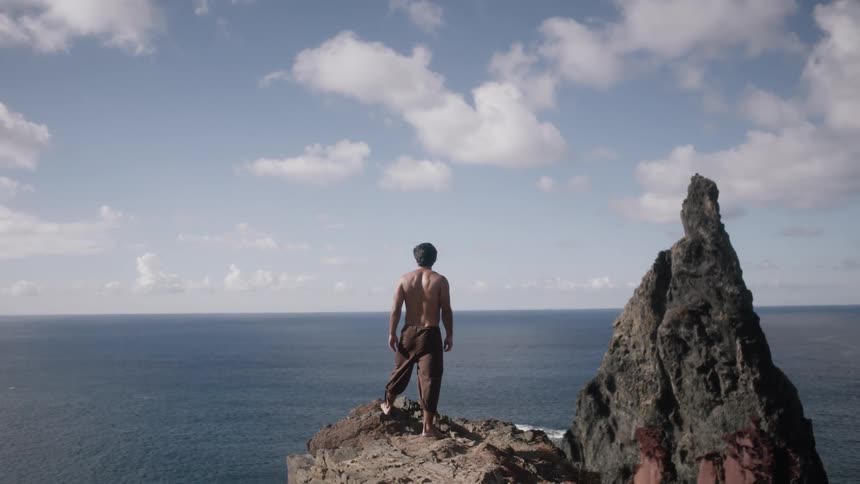 A man standing on the edge of a cliff looks out over the ocean