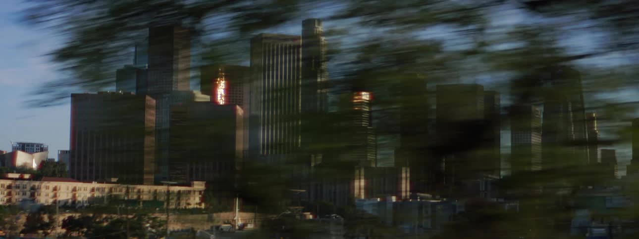 Tall downtown buildings and skyscrapers are seen from moving on a road in the distance