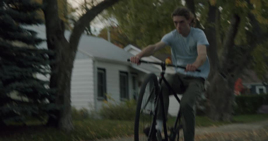 A man does a wheelie while riding a bicycle down a neighborhood street on an autumn day