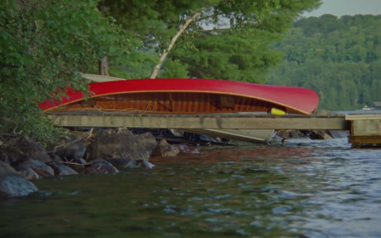 A canoe sits upside down on a pier over a fast moving river
