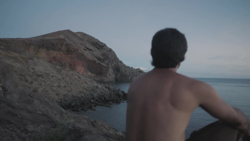 A man sits on a cliff overlooking the ocean
