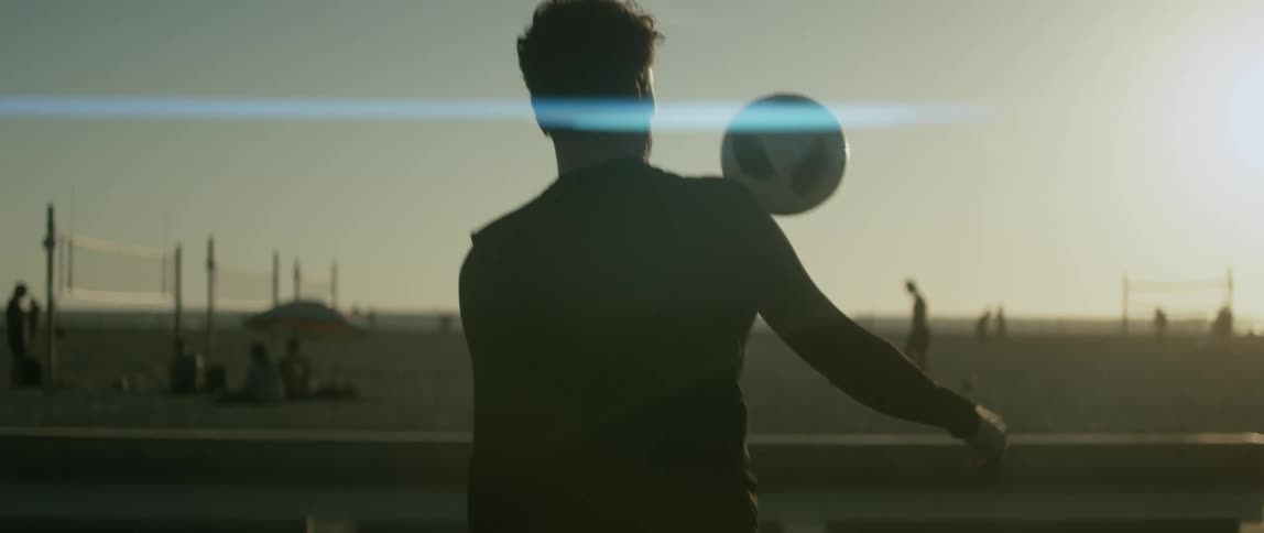 A man juggles a soccer ball with his legs on the beach during the day