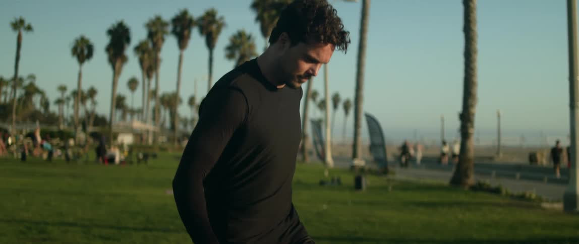 A man kicking around a soccer ball on a grassy lawn with palm trees in the distance